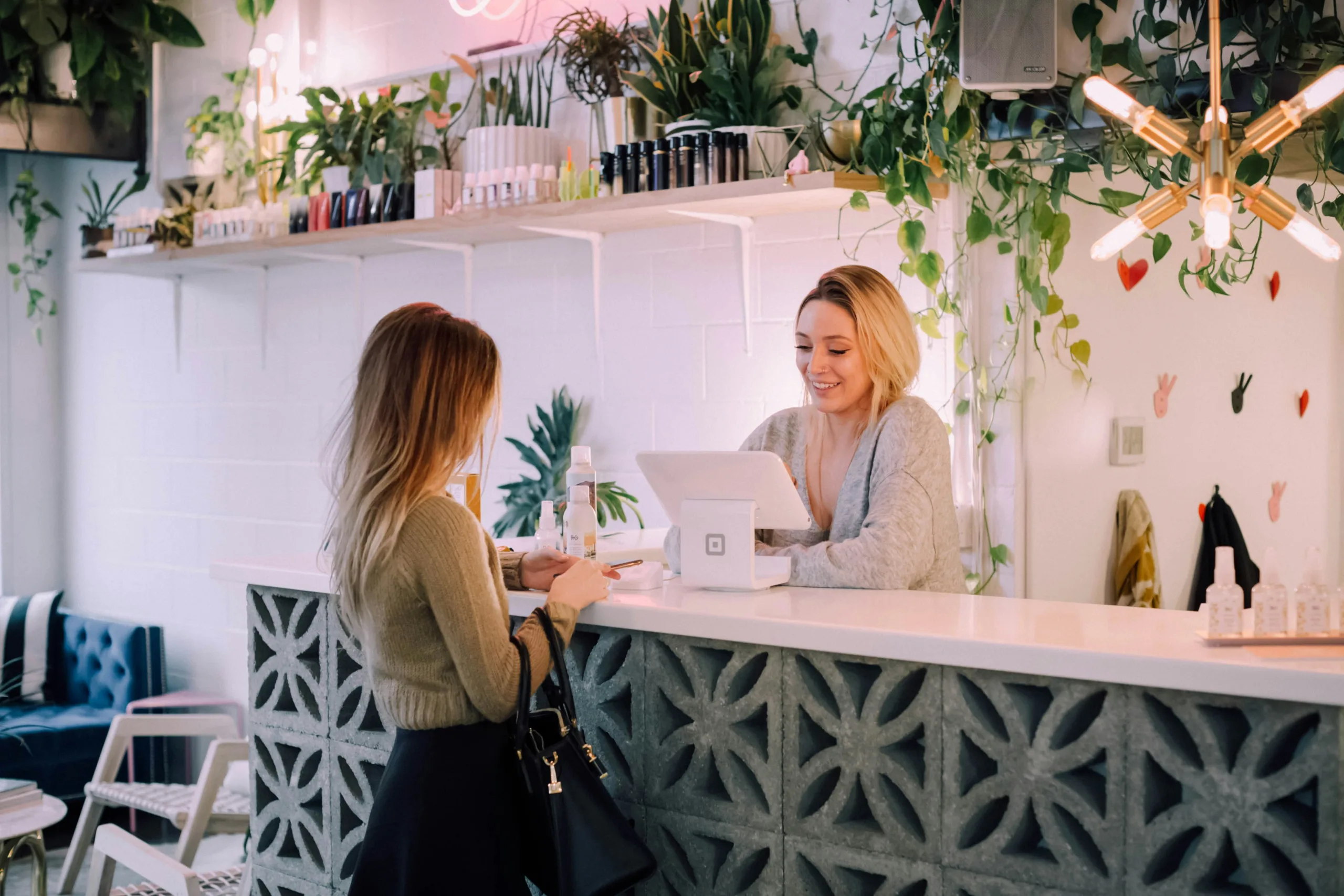 Woman at a retail counter interacting with a customer in a stylish, plant-filled space, highlighting local business engagement and customer service.
