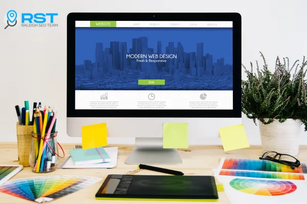 Desktop computer displaying a modern web design homepage with a blue skyline background, surrounded by colorful stationery and design tools, representing Raleigh SEO Team's Starter Website Package.